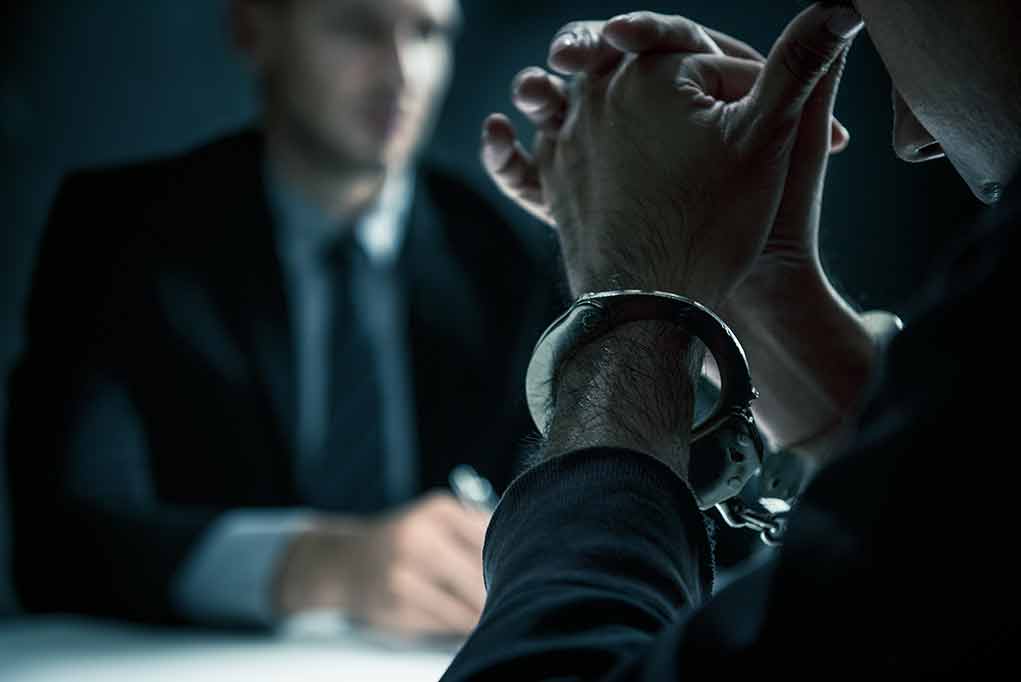 1117417790 featured image Handcuffed person in front of another individual.