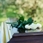 White roses on a polished wooden casket outdoors