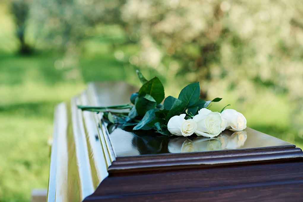 White roses on a polished wooden casket outdoors