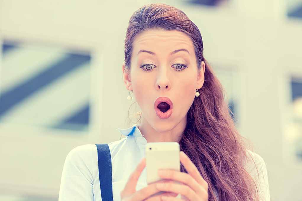 Surprised woman looking at her smartphone outdoors