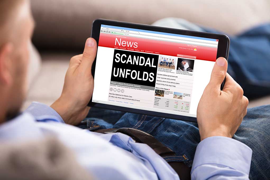 Person reading tablet with headline scandal unfolds