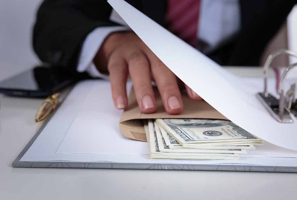Hand concealing cash under a folder on a desk