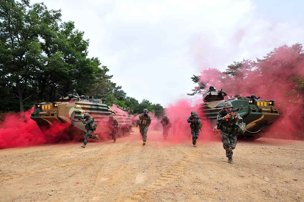 Soldiers running from armored vehicles with red smoke