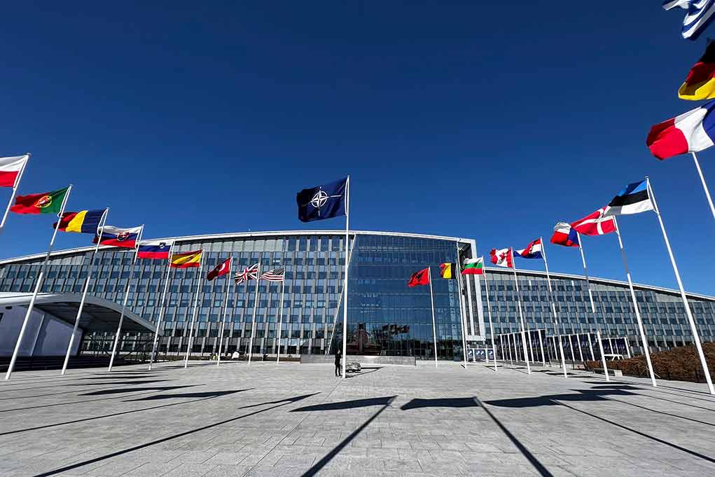 Flags outside NATO headquarters building under clear blue sky