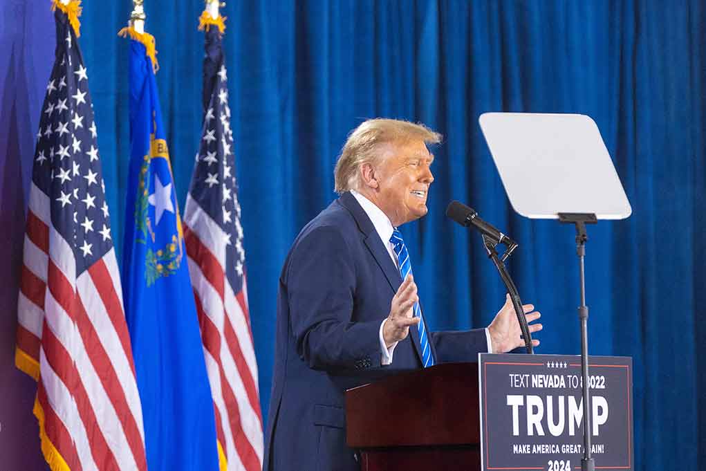 Person speaking at podium with flags in background