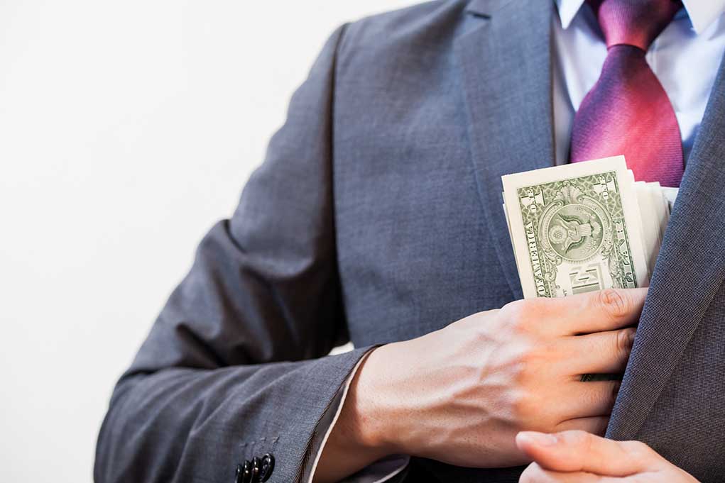Person in suit putting dollars in jacket pocket