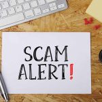 Scam alert message on a wooden desk.
