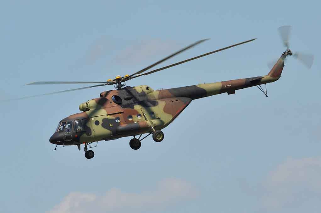 Camouflage military helicopter in flight against blue sky