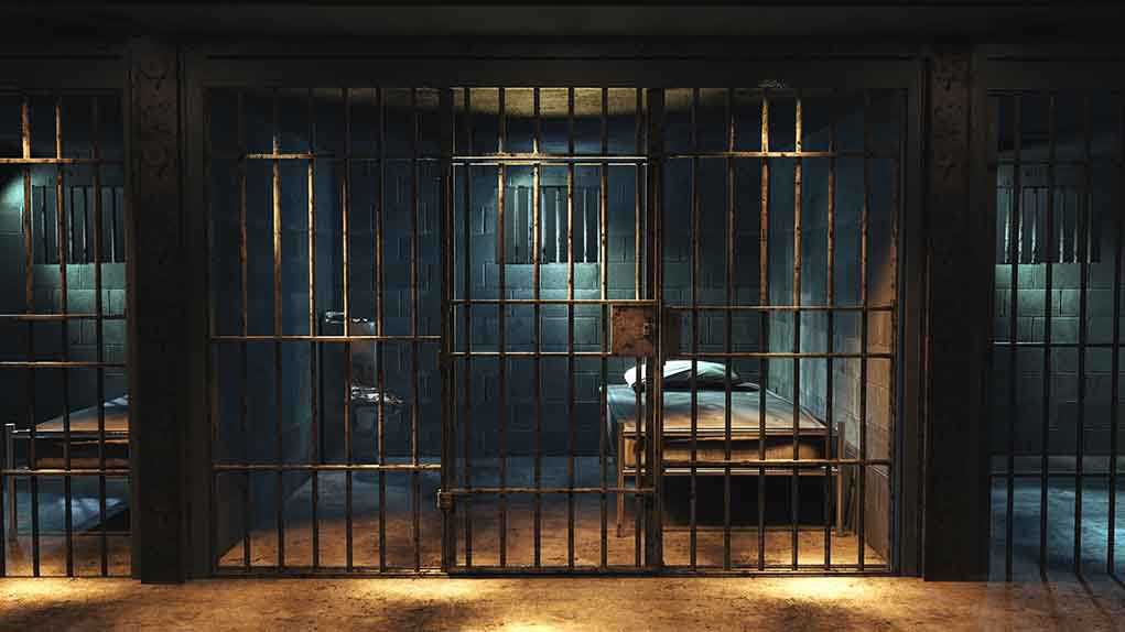 Empty prison cell with metal bars and bed