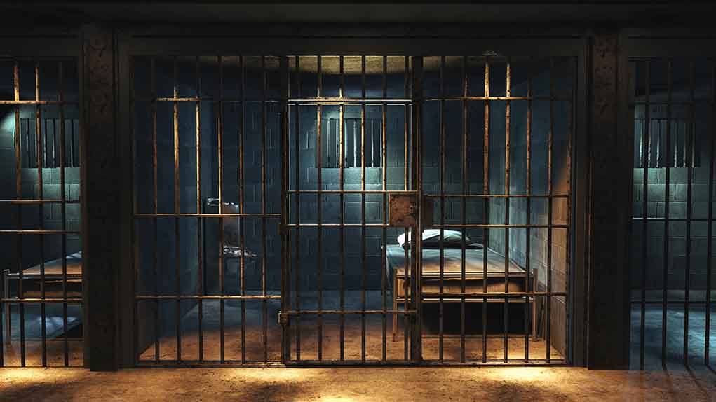 Empty prison cell with metal bars and bed