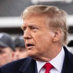Man in suit and red tie speaking outside