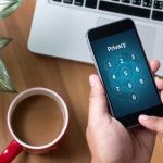 Kim’s Surveillance Tech SHOCKS Investigators Typing privacy passcode on smartphone near laptop and coffee