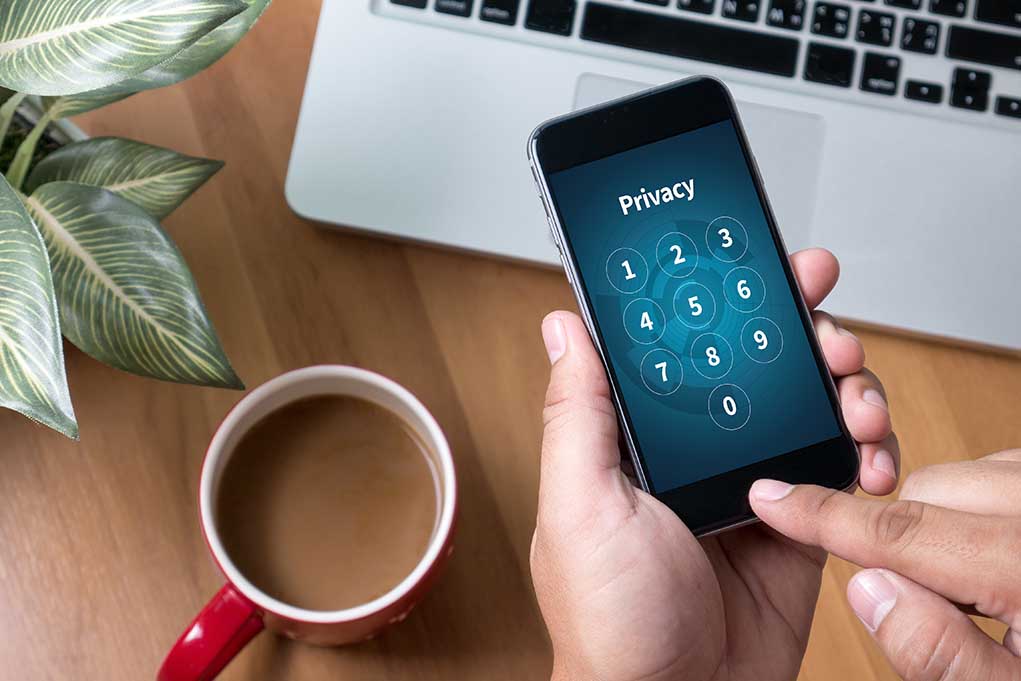 Typing privacy passcode on smartphone near laptop and coffee