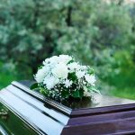FIERY Crash Kills Barrier-Breaking Female Pilot Coffin with white flowers outdoors in green surroundings