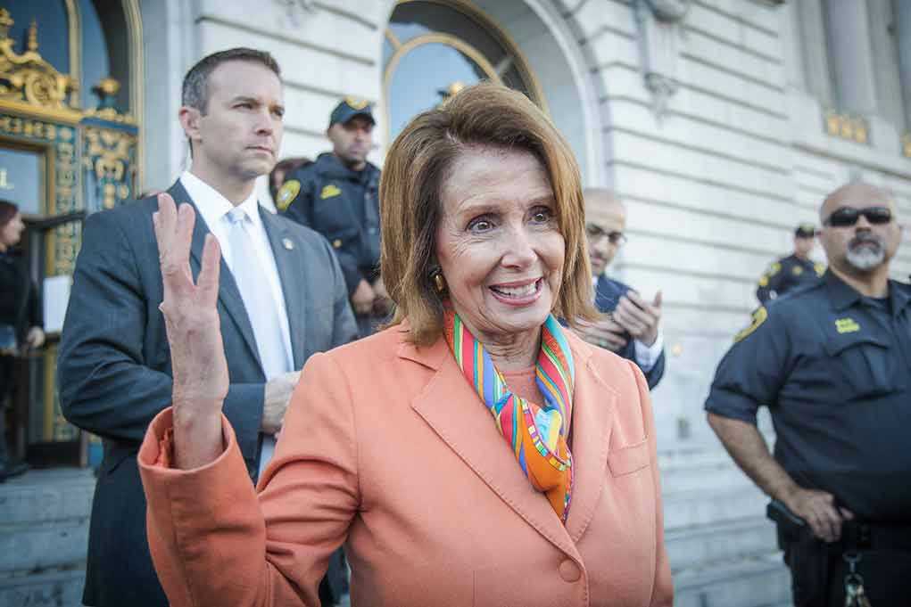 Woman in orange blazer speaking surrounded by security personnel