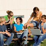 Group of students sitting on a bench outdoors, engaged in study and discussion