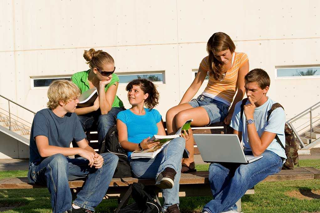 Group of students sitting on a bench outdoors, engaged in study and discussion
