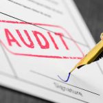 Audit stamp and pen signing a document