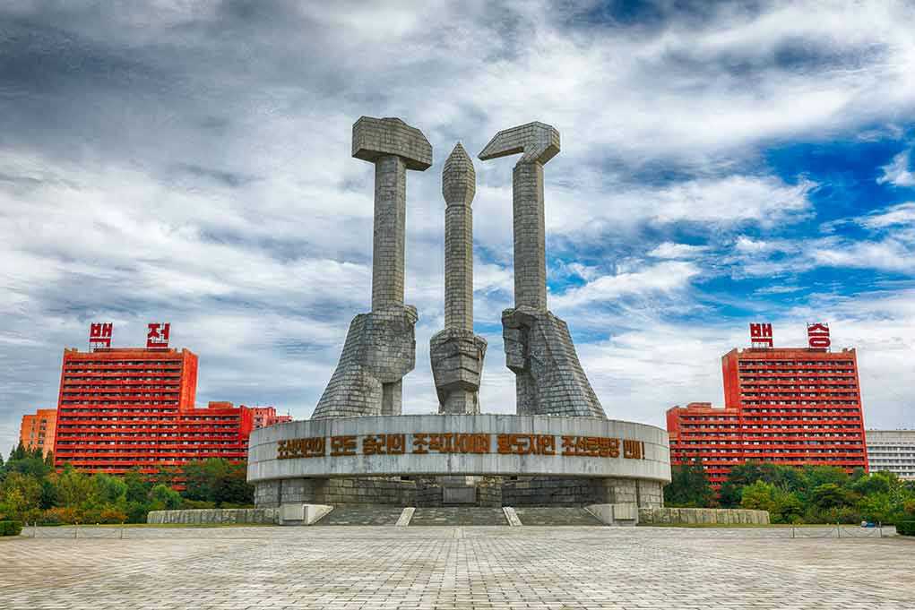 Concrete monument with hands holding tools under cloudy sky.