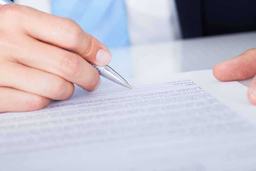 A hand holding a pen poised above a document for signing