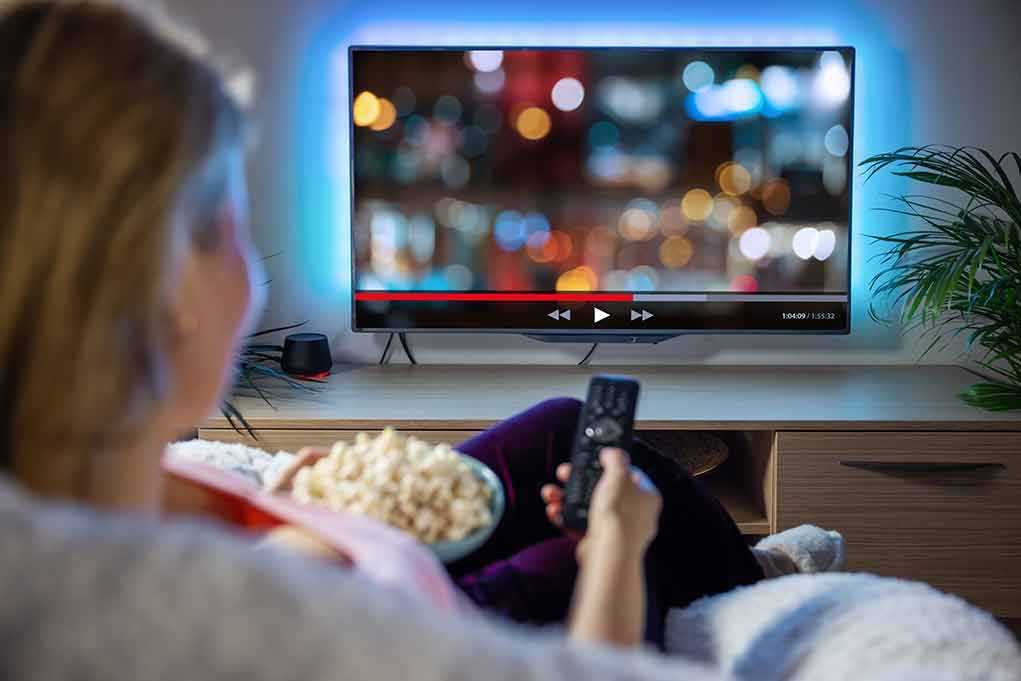 Person sitting on a couch watching a movie on a TV with popcorn in hand