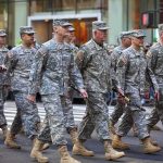 Group of soldiers marching in a military parade on a city street