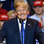 SOCIALIST Mayoral Candidate CHALLENGES Trump – Will He Accept? Man in suit speaking at rally with red hats.