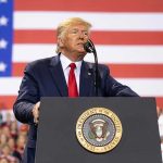 Trump’s Poland Troop Bombshell—Russia on Edge Man speaks at podium with U.S. flag background.