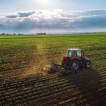 War Chemicals UNLEASHED on American Farms Tractor plowing a vast green field at sunset.