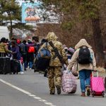 Bomb Panic—City Evacuates Overnight Group of people carrying luggage walking along a road with a soldier