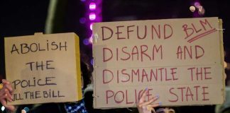 Two individuals holding protest signs with messages about police reform