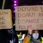 BLM Star BROUGHT DOWN in Million-Dollar Scam Two individuals holding protest signs with messages about police reform