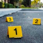 Two Sisters ARRESTED — Three Students DEAD! Crime scene markers on asphalt with bullet casing.