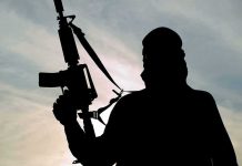 Silhouette of a person holding a rifle against a cloudy sky