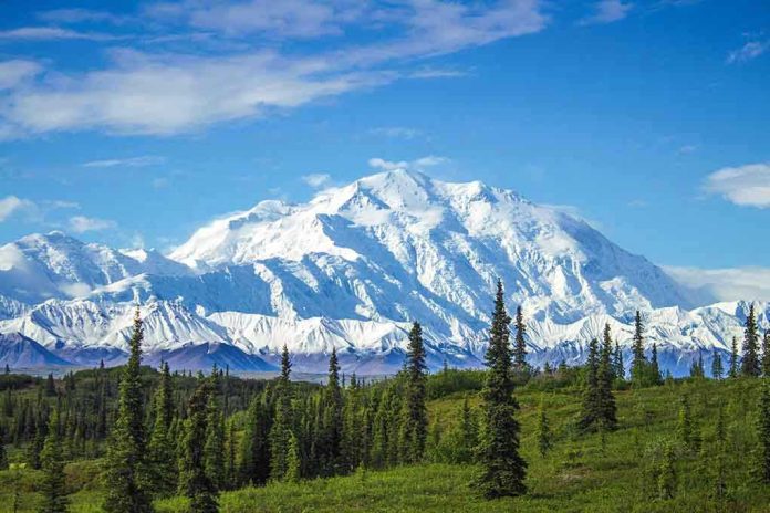 1068590996 Snow-covered mountain under blue sky with green foreground.
