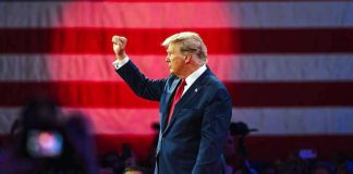 Person in suit with fist raised in front of flag.