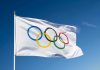 IOC Drops Bombshell — Ban Shakes Olympics Olympic flag waving against clear blue sky.
