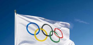 Olympic flag waving against clear blue sky.