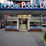 NYPD precinct building with signs on a city street
