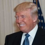 A smiling man in formal attire with an American flag in the background