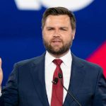 Man in a suit speaking at an event.