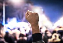 Massive UPRISING -This Government Just Got Toppled! Raised fist in a crowd at night.