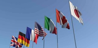 Flags of seven countries against clear blue sky.