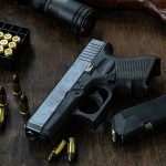 Warnings Ignored Before School Attack Handgun with ammunition, magazine, and rifle on wooden table.