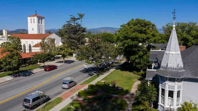 Street with church, parked cars, and trees.