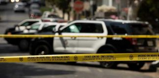 Police tape blocking street with patrol cars.