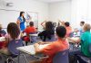 Teacher in a blue dress instructing students in a classroom with hands raised