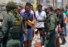 $5.7B In Migrant Aid SLASHED Border patrol agents inspecting group of individuals in line.