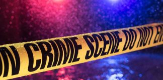 Yellow crime scene tape with police lights in background.