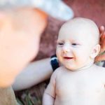 A smiling baby interacting with a parent in a military uniform
